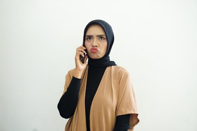 Retrato de uma triste mulher muçulmana asiática usando hijab fazendo uma ligação com um telefone celular