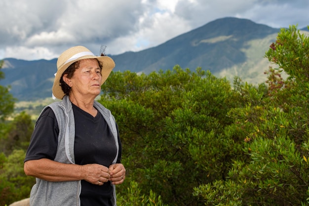 Retrato de uma velha agricultora latina no campo com arbustos e montanhas ao fundo