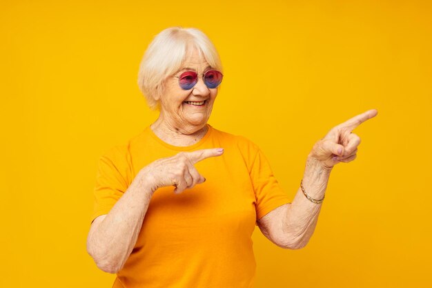 Retrato de uma velha amigável em óculos de sol de camiseta casual fundo amarelo