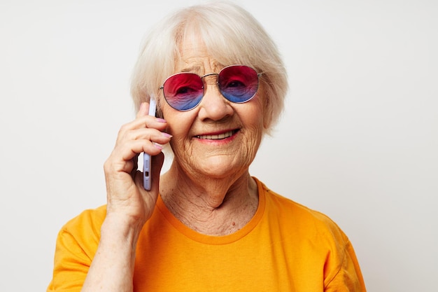 Retrato de uma velha amigável em uma camiseta amarela, posando comunicação por telefone, emoções fechadas