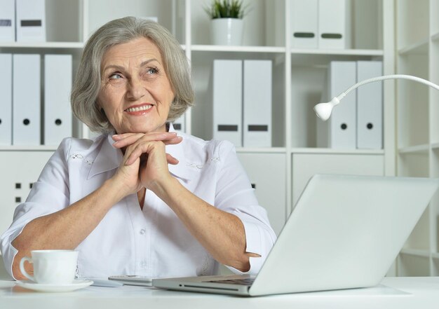 Retrato de uma velha mulher de negócios usando laptop no escritório