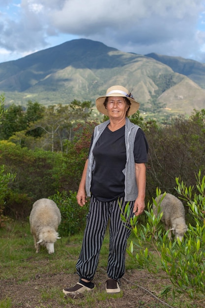 Retrato de uma velha pastora latina no campo com seus arbustos de ovelhas e montanhas ao fundo