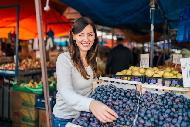 Retrato de uvas de compra de uma jovem mulher no mercado de rua. Olhando para a câmera.