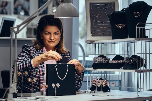 Retrato de vendedora elegantemente vestida embala brincos preciosos em uma caixa para seu cliente em uma joalheria de luxo.