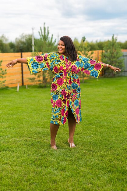 Retrato de verão da bela mulher afro-americana em vestido colorido em pé no estilo de vida suburbano do quintal e relaxando no fim de semana no campo e inclusão com o conceito de diversidade