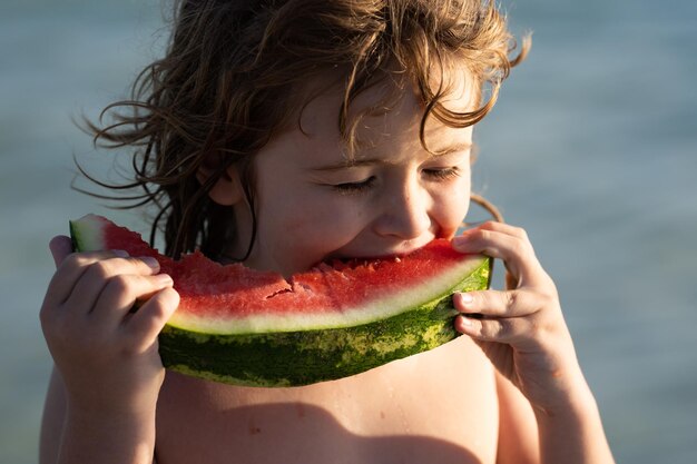 Retrato de verão de criança fofa brincando na praia e comendo melancia pequeno menino mordendo