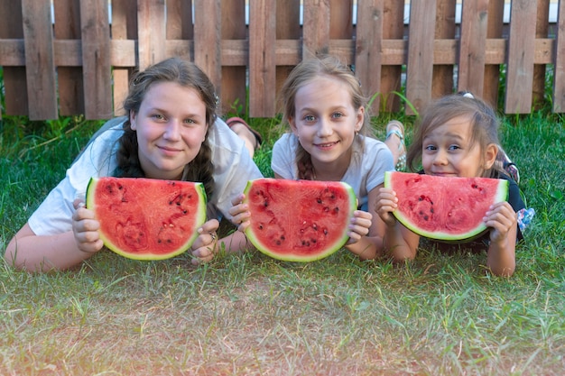 Retrato de verão de três irmãs. crianças sorridentes ao ar livre. crianças com melancia. três criança feliz e sorridente comendo melancia no parque. conceito de verão.