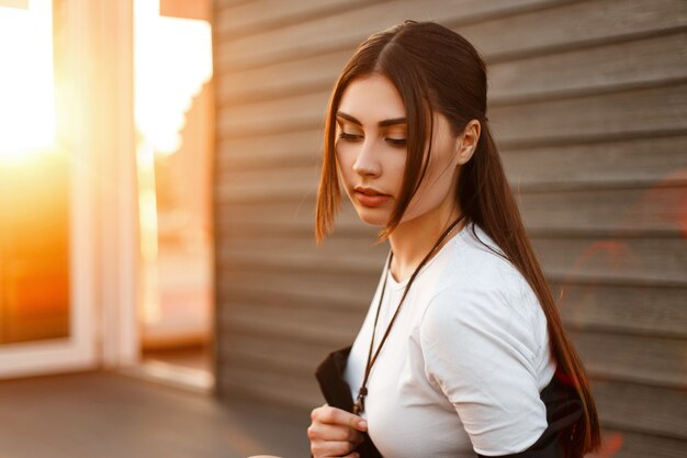 Retrato de verão de uma bela jovem com roupas da moda ao pôr do sol