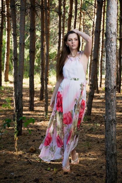 Retrato de verão de uma linda jovem garota de vestido em uma floresta de pinheiros