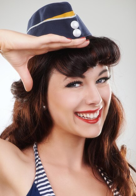 Foto retrato de viagem e saudação de uma marinheira e modelo em estúdio isolado em um fundo branco sorriso pin up e rosto de hospedeira de avião vintage em maquiagem de chapéu e pin up girl na espanha para moda