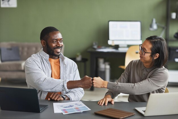 Retrato de vista frontal de dois empresários étnicos afro-americanos e asiáticos batendo durante o trabalho