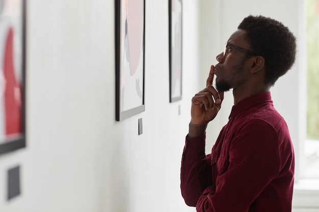 Retrato de vista lateral de um jovem afro-americano olhando pinturas e pensando em uma galeria de arte ou exposição em museu,