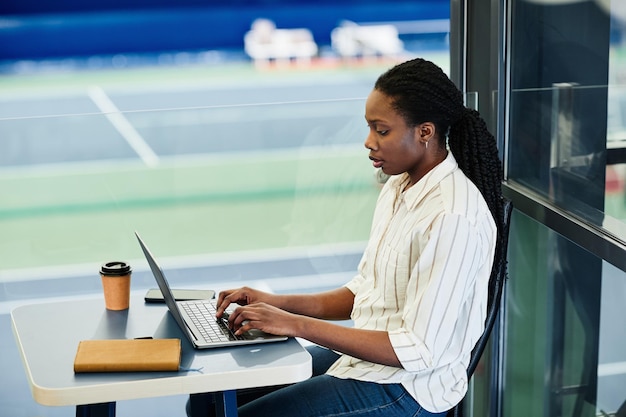 Retrato de vista lateral de uma jovem negra usando laptop enquanto trabalhava no centro de treinamento esportivo