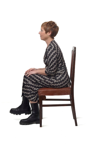Retrato de vista lateral de uma mulher de vestido e botas sentada na cadeira com pernas cruzadas sobre fundo branco