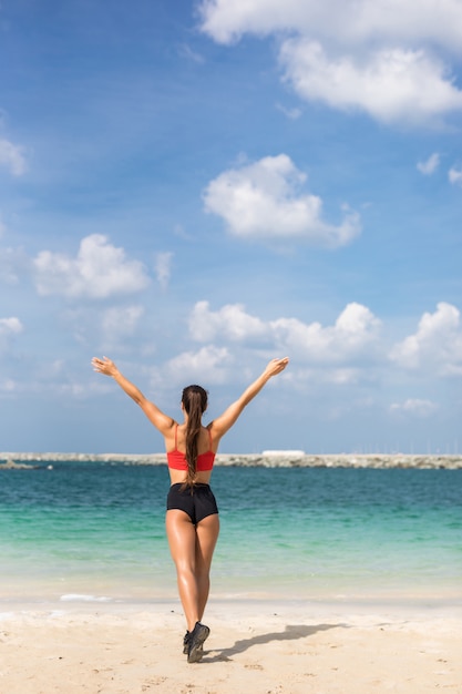 Retrato de vista traseira da mulher de fitness, esticando com as mãos levantadas na praia