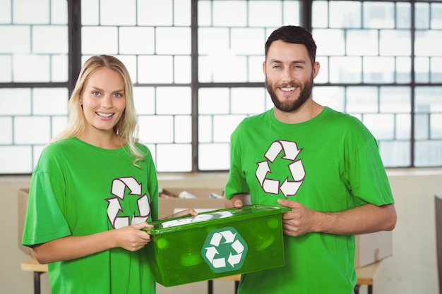 Retrato de voluntários sorridentes que transportam o recipiente de reciclagem