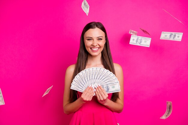 Retrato dela bonita atraente adorável alegre alegre garota de cabelos compridos segurando nas mãos uma grande quantia de dinheiro isolada em um fundo de cor rosa fúcsia vibrante brilho vívido brilhante