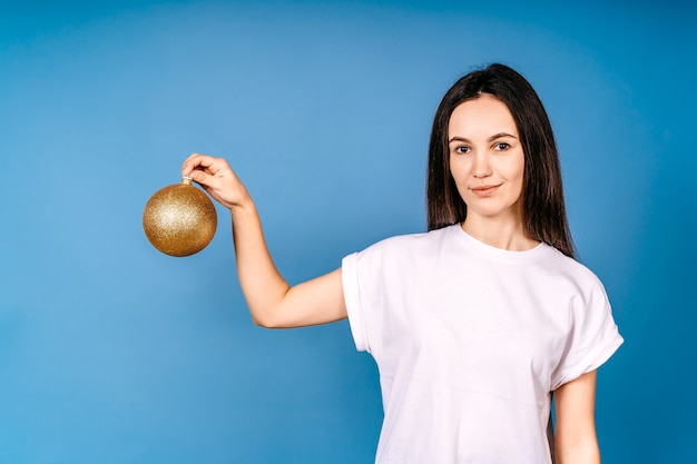 Retrato dela, ela é legal, atraente, charmosa, alegre, alegre, menina, segurando nas mãos bola dourada brilhante brinquedo do abeto de ano novo tradição festiva isolada brilhante brilho vívido parede azul vibrante