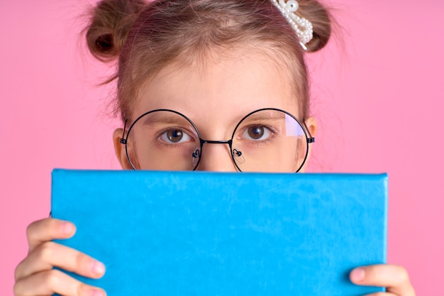 Retrato dela ela linda raposa adorável atraente alegre positiva menina da escola segurando nas mãos, se escondendo atrás da preparação para o exame de livro aberto isolada sobre o espaço rosa