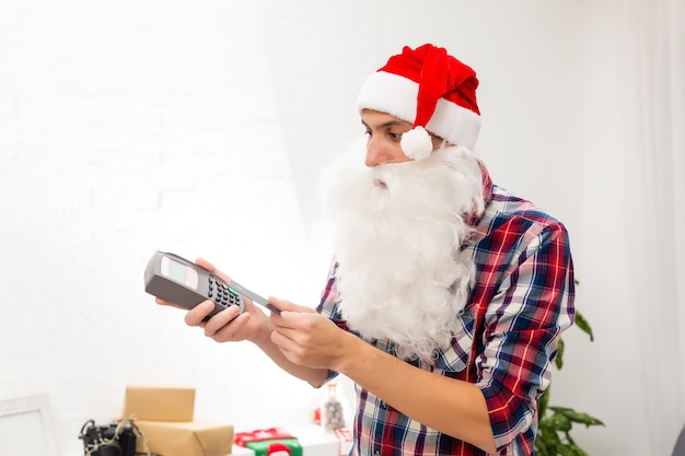 Retrato dele, ele é simpático e atraente, alegre e gordo Papai Noel segurando nas mãos e carregando coisas com terminal digital, loja de varejo, cartão de pagamento da boutique