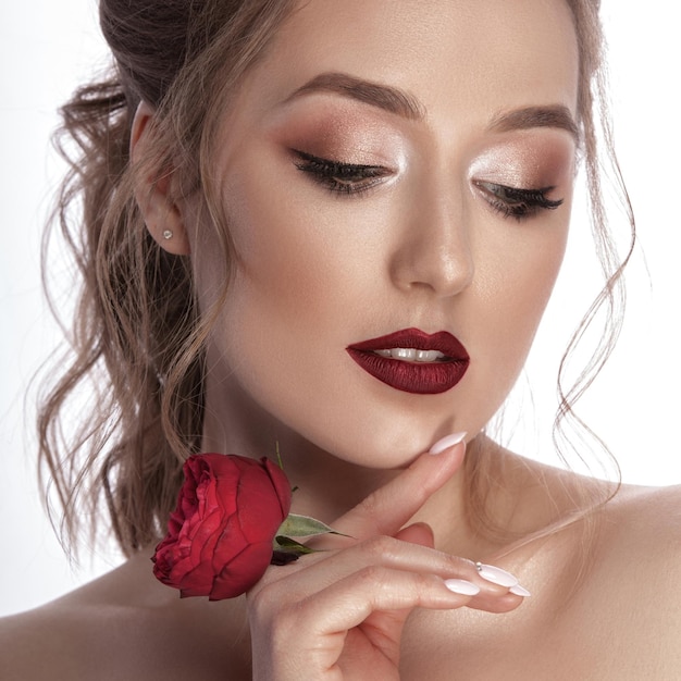 Retrato delicado e glamoroso de uma jovem com uma flor vermelha nas mãos Bela maquiagem e penteado Fundo isolado branco fotografado