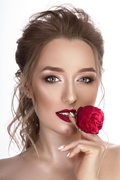 Retrato delicado e glamoroso de uma jovem com uma flor vermelha nas mãos Bela maquiagem e penteado Fundo isolado branco fotografado