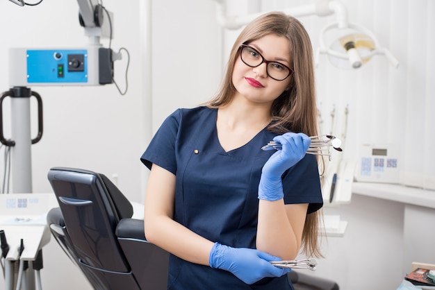 Retrato del dentista amistoso joven que sostiene los instrumentos dentales en la oficina dental moderna.