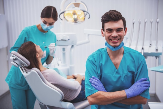 Retrato de un dentista feliz con una máscara y guantes en el fondo del asistente que trata al paciente de dientes