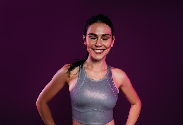 Retrato de una deportista alegre con ropa de fitness plateada contra un telón de fondo magenta