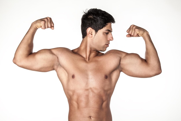 Retrato de un deportista atlético fuerte posando sin camisa, demostrando un cuerpo hermoso, mostrando sus brazos, jactándose de bíceps, mirando hacia otro lado. Disparo de estudio interior aislado sobre fondo blanco.