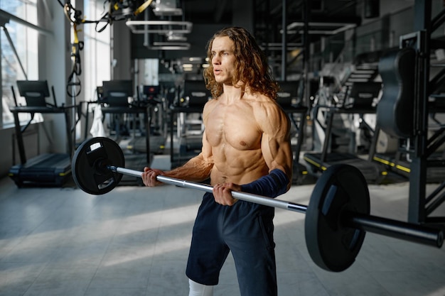 Retrato de deportista fuerte con cuerpo musculoso perfecto haciendo ejercicios con barra. Entrenamiento entrenamiento de culturismo en el gimnasio