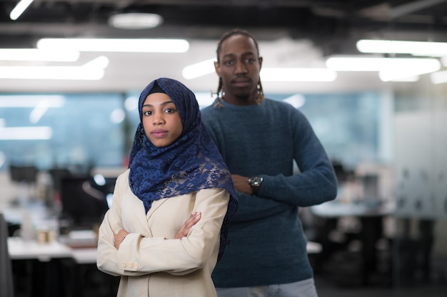 Retrato de desarrollador de software femenino musulmán negro de pie junto con su colega afroamericano en la moderna oficina de inicio