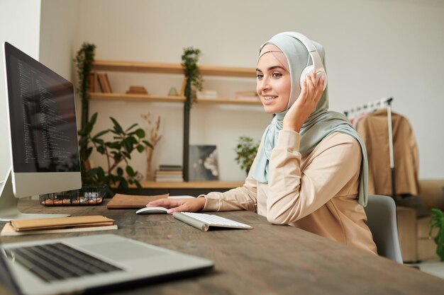 Retrato de un desarrollador de software profesional que usa hiyab y auriculares sentado en el escritorio con onli