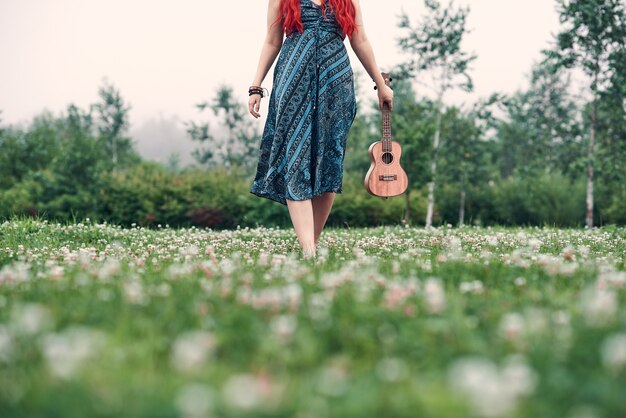 Foto retrato despersonalizado de mujer con ukelele caminando en un claro de verano en el parque.