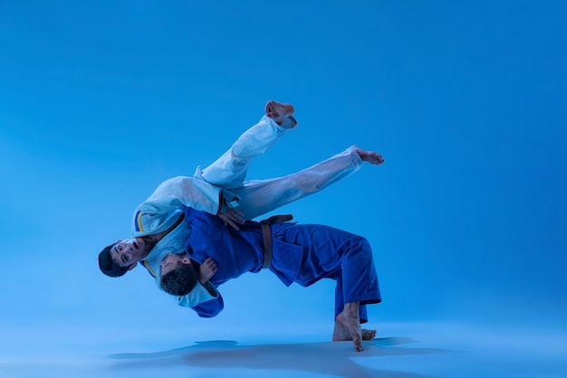 Retrato dinámico de atletas profesionales de judo entrenando aislado sobre fondo de estudio azul en neón