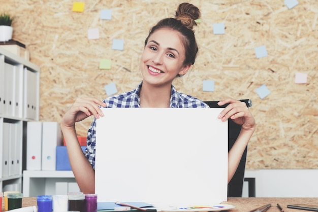 Foto retrato de una diseñadora alegre en el trabajo. está sentada en la oficina de su casa con una camisa a cuadros azul y trabajando con bocetos. imagen tonificada. bosquejo