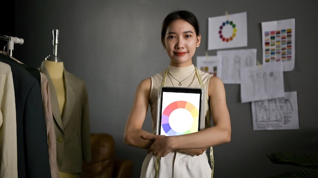 Retrato de una diseñadora de moda asiática segura de sí misma sosteniendo su tableta con una tabla de colores en la pantalla