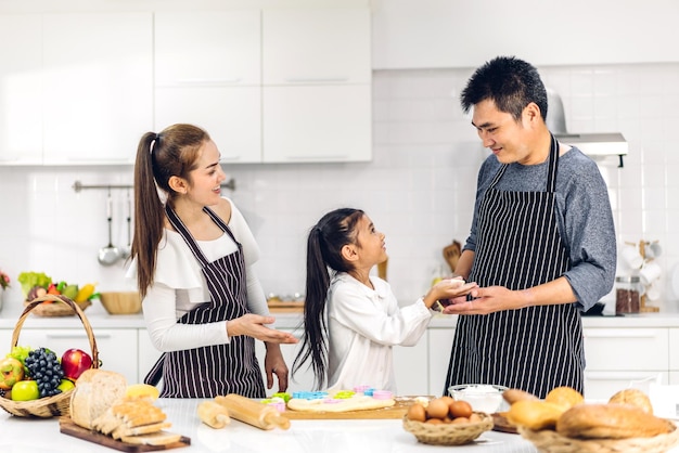 Retrato de disfrutar del amor feliz familia asiática padre y madre con niña asiática hija jugar y divertirse cocinando comida junto con hornear galletas e ingredientes para pasteles en la cocina