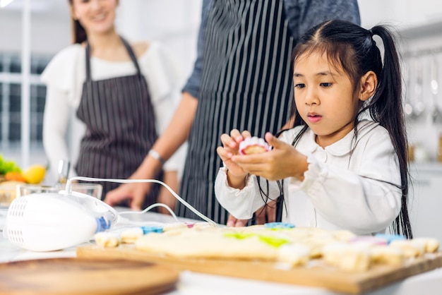 Retrato de disfrutar del amor feliz familia asiática padre y madre con niña asiática hija jugar y divertirse cocinando comida junto con hornear galletas e ingredientes para pasteles en la cocina