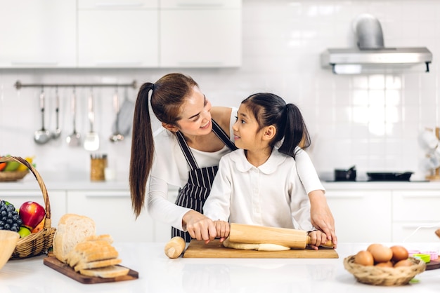 Retrato de disfrutar de amor feliz madre de familia asiática y niña asiática hija niño divirtiéndose cocinando junto con hornear galletas e ingredientes de pastel en la mesa en la cocina