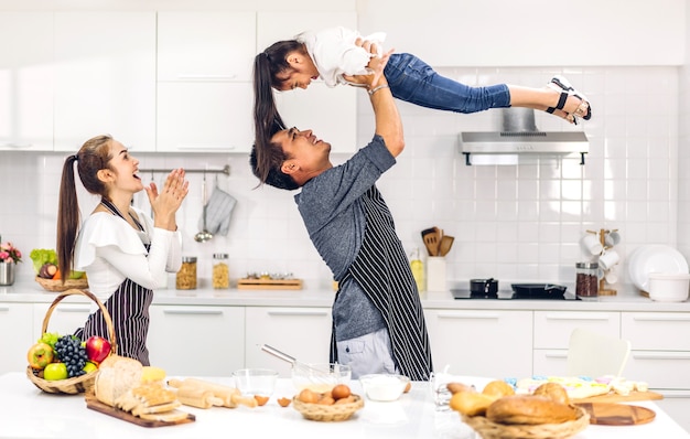 Foto retrato de disfrutar del amor feliz padre de familia asiática y madre con niña asiática hija niño divirtiéndose cocinando junto con hornear galletas e ingredientes de pastel en la mesa en la cocina