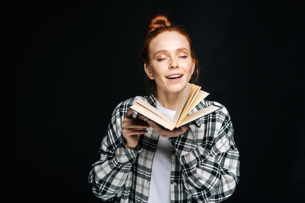 Retrato de disfrutar de una joven estudiante universitaria de pie con los ojos cerrados sosteniendo un libro abierto