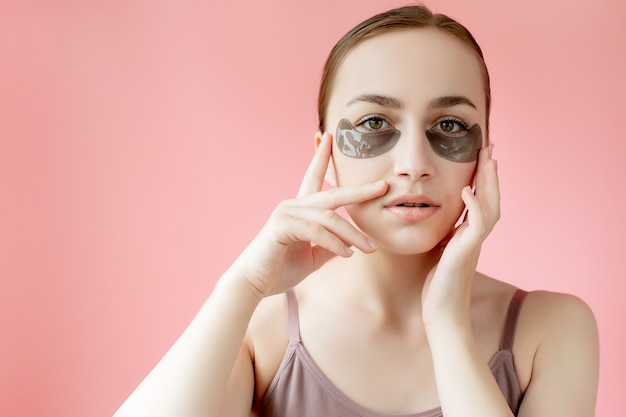 Retrato de disparo a la cabeza de cerca a mujer joven sonriente con máscara de parches hidratantes debajo de los ojos mirando a cámara disfrutando del procedimiento de cuidado de la piel.