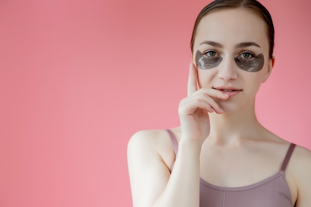 Retrato de disparo a la cabeza de cerca a mujer joven sonriente con máscara de parches hidratantes debajo de los ojos mirando a cámara disfrutando del procedimiento de cuidado de la piel.