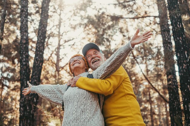 Retrato de disparo en la cabeza de cerca de personas alegres de mediana edad sonriendo y mirando los árboles del bosque a su alrededor Anciana activa abriendo los brazos con su esposo abrazándola desde atrás