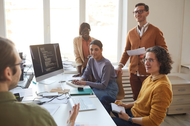 Retrato de diverso equipo de desarrollo de TI discutiendo el proyecto y sonriendo mientras disfruta del trabajo en la producción de software, copie el espacio