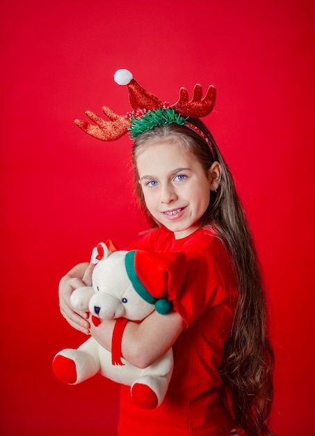 Retrato de una divertida niña alegre con vendaje de cuernos en la cabeza abrazando fondo rojo aislado