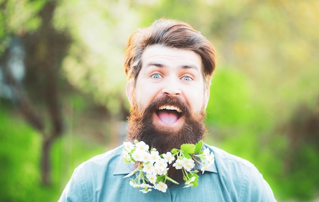 Retrato divertido de la cabeza de la barba de flor de un hombre barbudo mirando a la cámara sobre el fondo de la flor de primavera