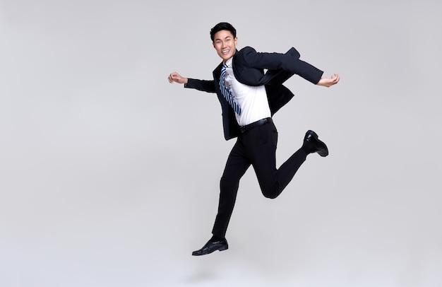 Retrato divertido de feliz enérgico jovem empresário asiático, saltando no ar em branco do estúdio.