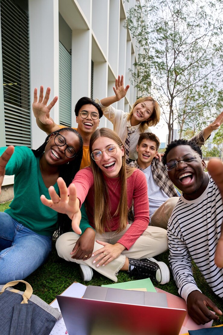 Foto retrato divertido de um grupo de jovens amigos diversos animados acenando para a câmera com as mãos sentadas na grama